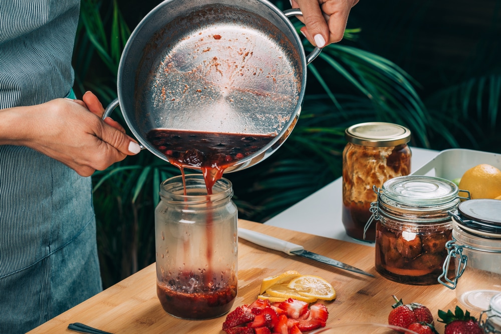 A view of a person pouring strawberry jam into a jar for canning