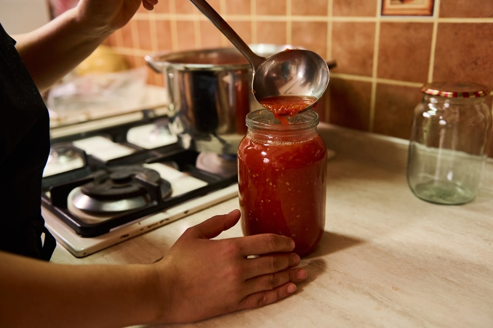 A view of stewed tomatoes being poured into a glass jar