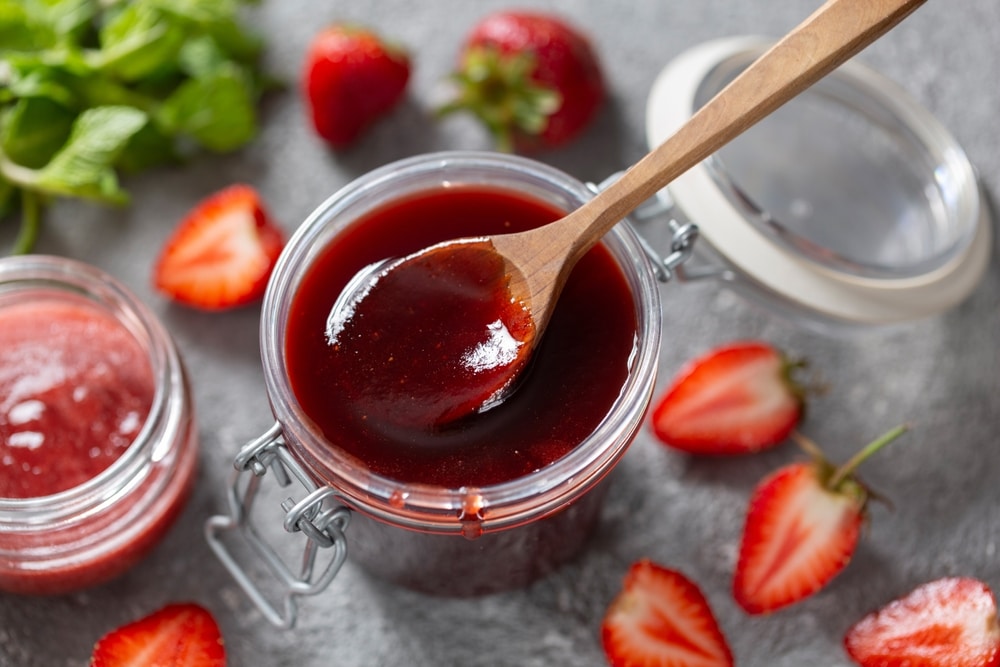 An overhead view of strawberry jam in a can with a ladle inside