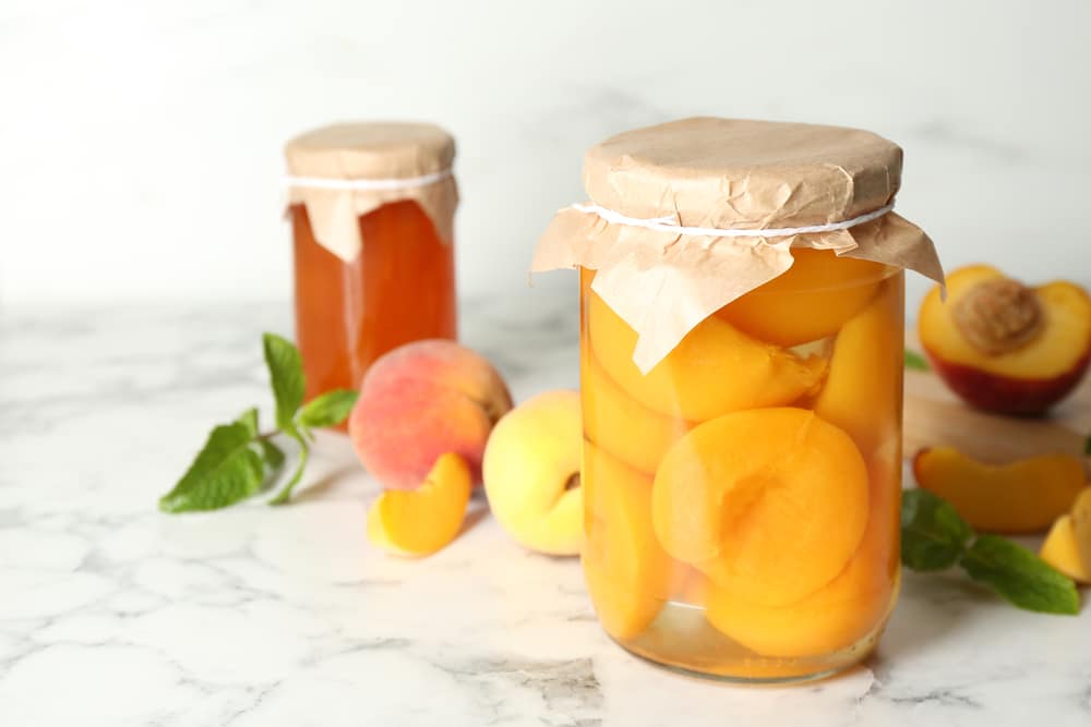 Glass Jar Of Pickled Peaches And Fresh Fruits On White