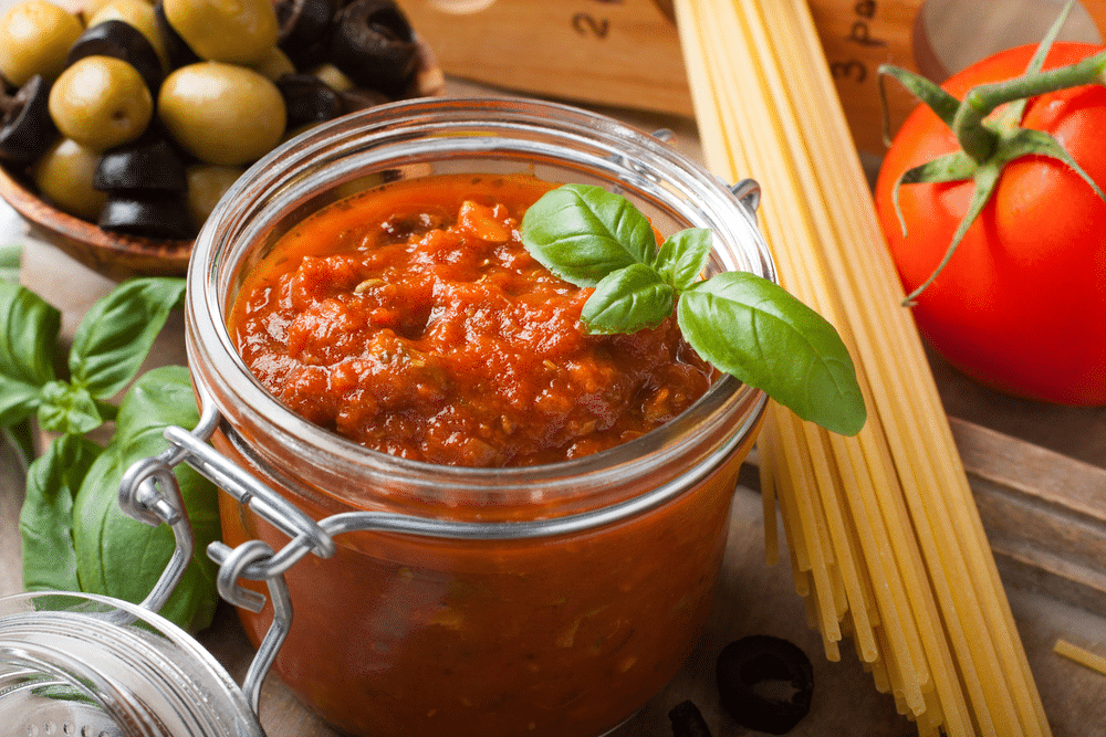 Glass jar with homemade classic spicy pasta sauce with olives and basil