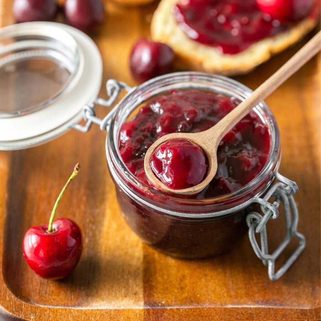 A top view of cherry jam inside a mason jar with a wooden spoon