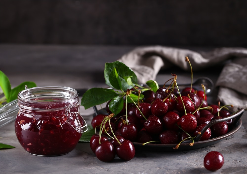 A view of a cherry jam pot with cherries on the side