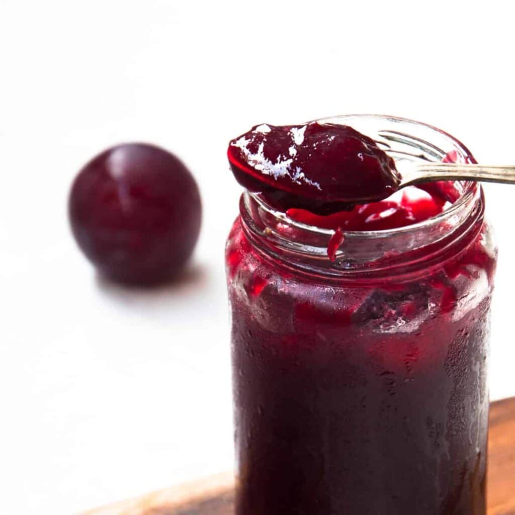 A view of a dark purple plum jam inside a glass jar with a spoonful