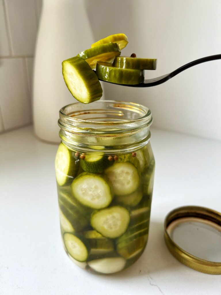 A view of a fork taking out sliced pickled cucmbers out of a jar