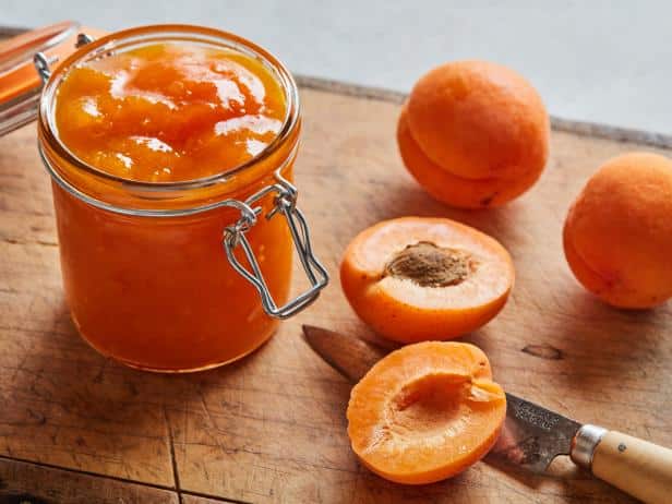 A view of apricot jam in a jar with a half cut apricot and a knife