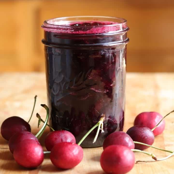 A view of cherry jam in a mason jar with cherries alongside