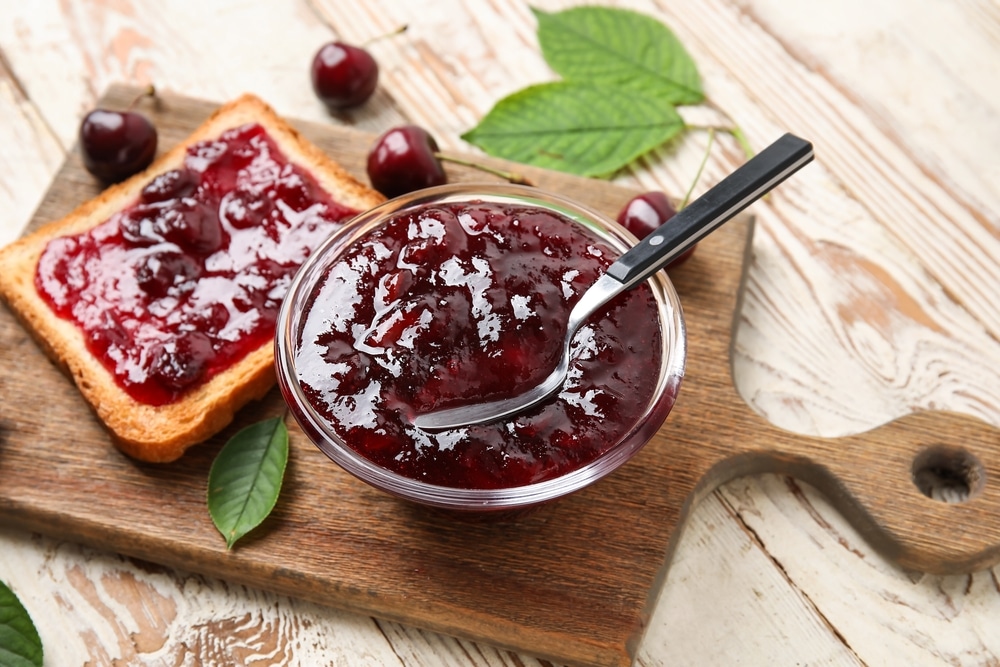 A view of cherry jam inside a bowl and spread on toast