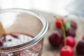 A view of cherry jam on a loaf of bread alongside a jam bowl