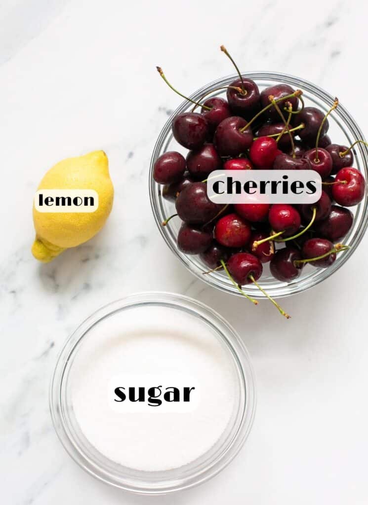 An overhead view of ingredients of cherry jam; a lemon sugar and some cherries in a bowl