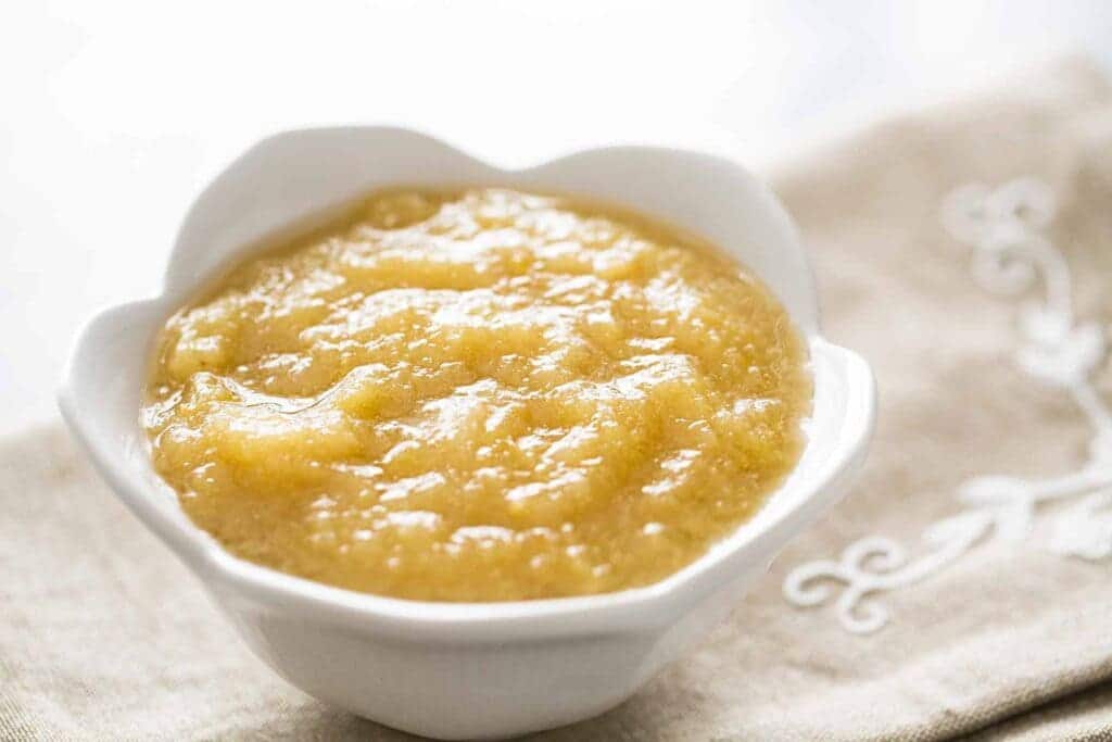 a white bowl of applesauce placed on a cloth