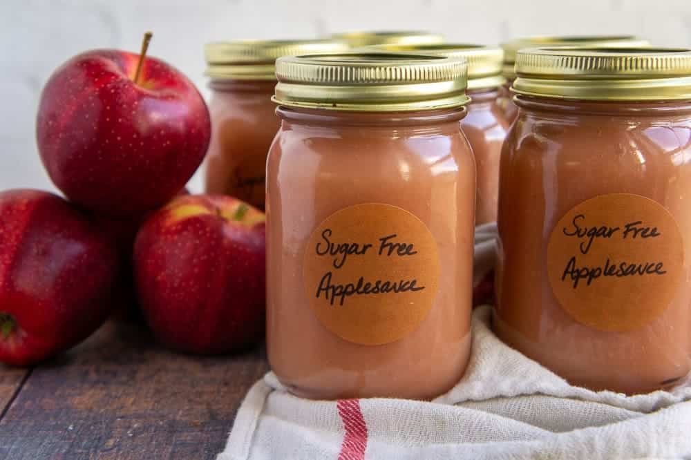 jars of apple sauce with apples placed on a wooden surface