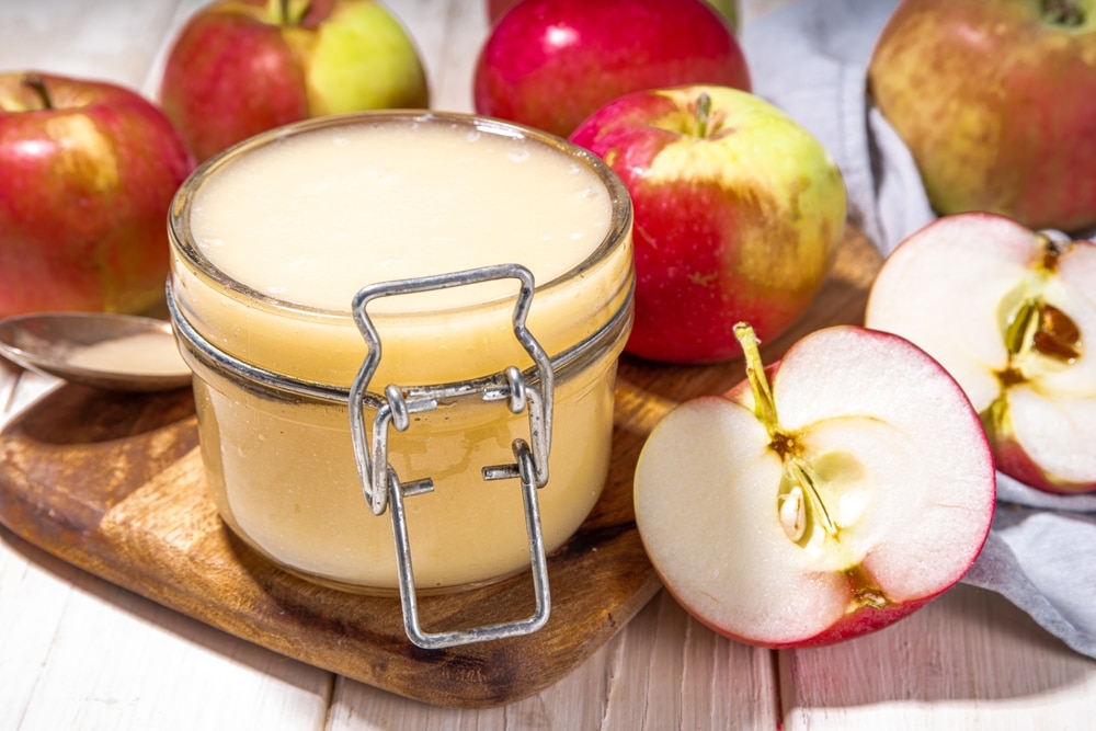 apple sauce in small jar with fresh summer apples on wooden white background