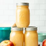 jars of apple sauce placxed on a cloth with an apple