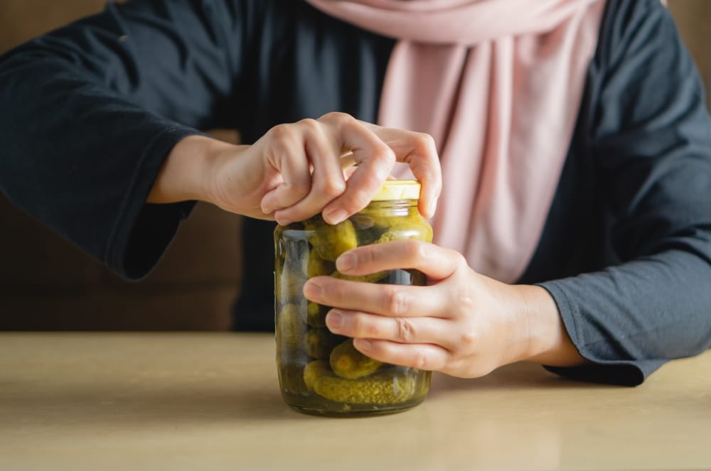 A Woman Tries To Open A Jar Of Pickles With