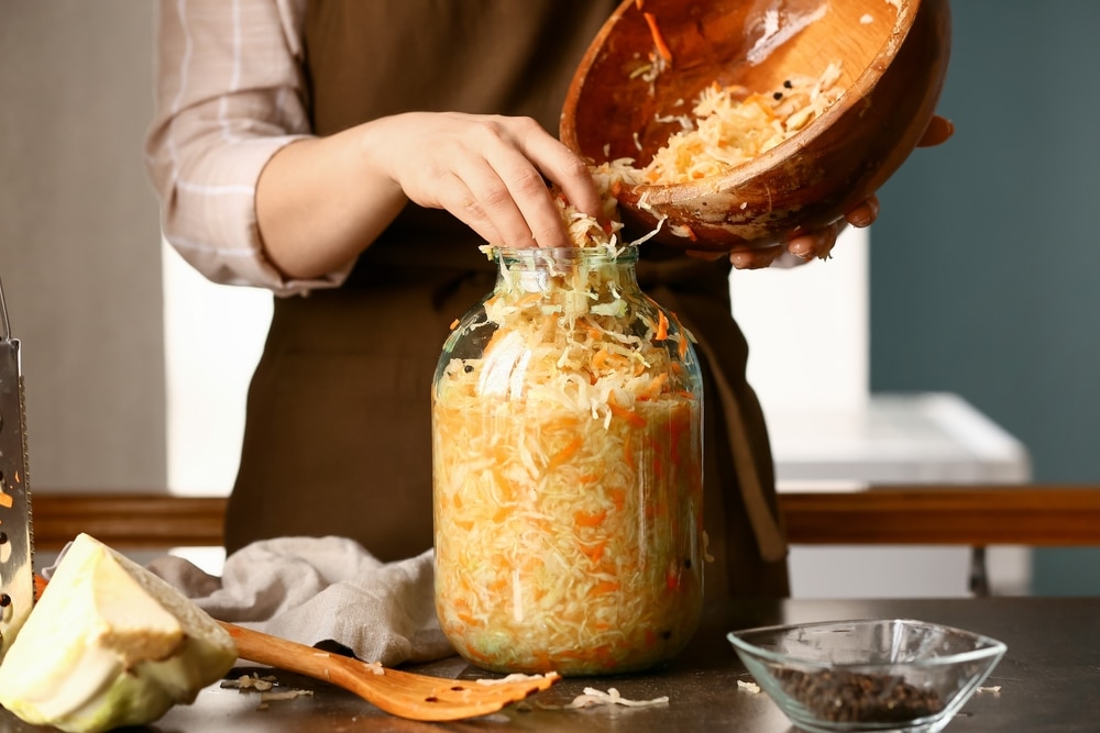 Woman Putting Tasty Sauerkraut Into Glass Jar On Table In