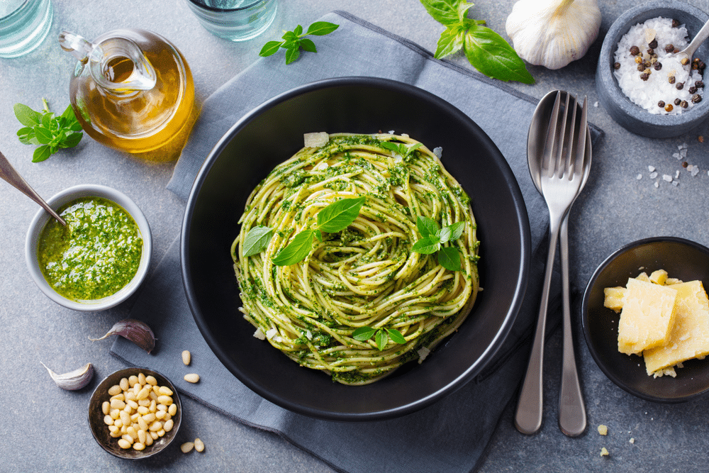 Pasta spaghetti with green tomato sauce and fresh basil leaves in black bowl Grey background Top view