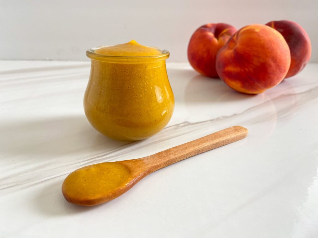 A view of peach puree in a glass jar with peaches on the side A view of peach puree in a glass jar with peaches on the side