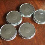 Five metal jar lids arranged on a wooden surface