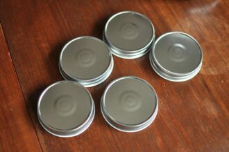 Five metal jar lids arranged on a wooden surface