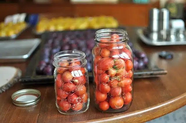 Two canning jars filled with tomatoes placed on a wooden surface