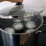 A person tightly securing the lid on a jar filled with pickles or other preserved items
