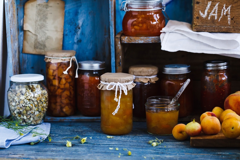Homemade jams and preserves in jars with fabric topped lids on a wooden shelf Homemade jams and preserves in jars with fabric topped lids on a wooden shelf