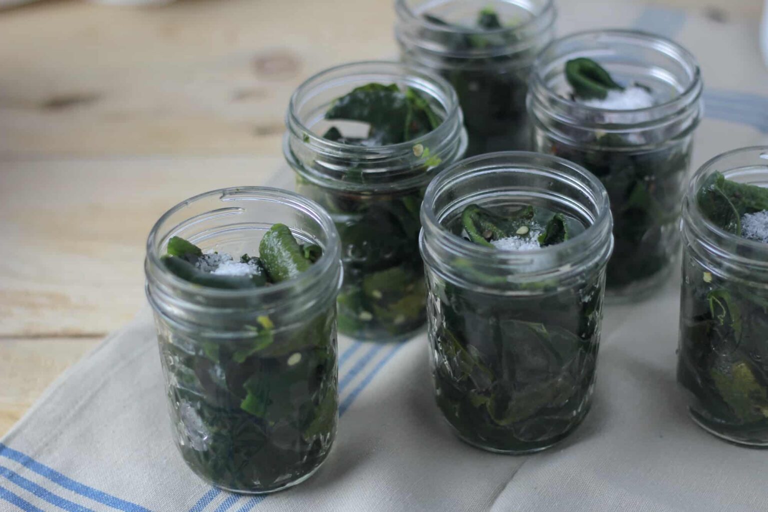 The image shows several jars filled with green peppers topped with salt ready for canning